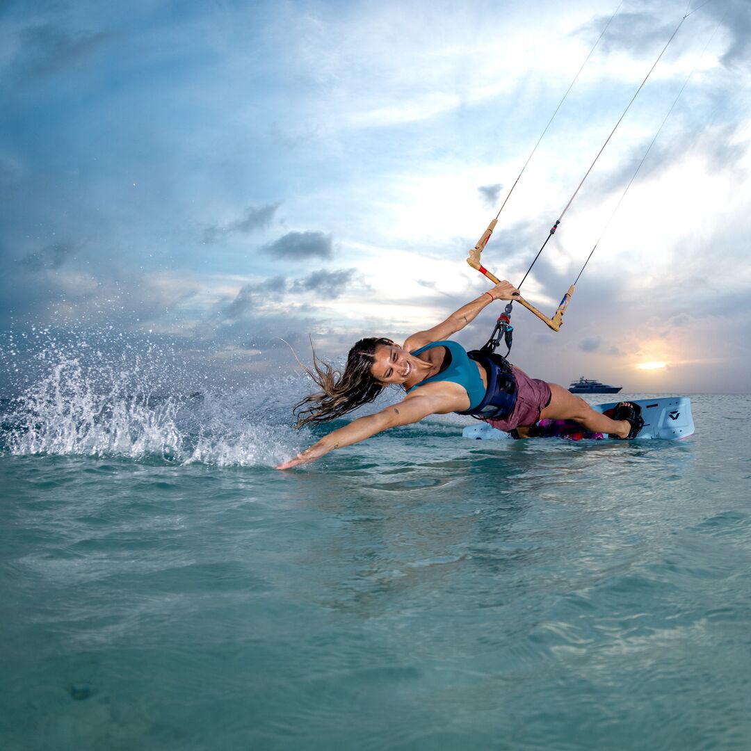Kitesurfeuse ridant avec la planche Duotone Soleil SLS 2026, figure stylée au coucher du soleil sur une eau turquoise.